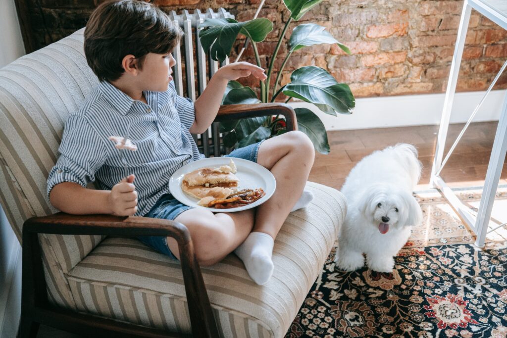 dog standing next to boy eating
